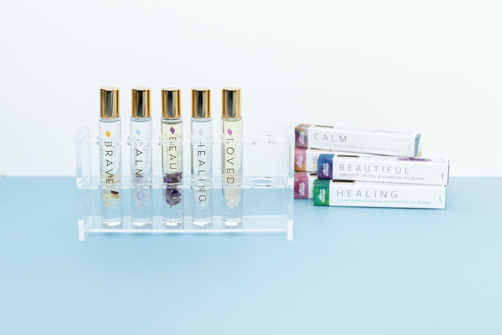 An acrylic roller bottle holder display holding 5 crystal roller bottles with essential oils with their boxes in the background