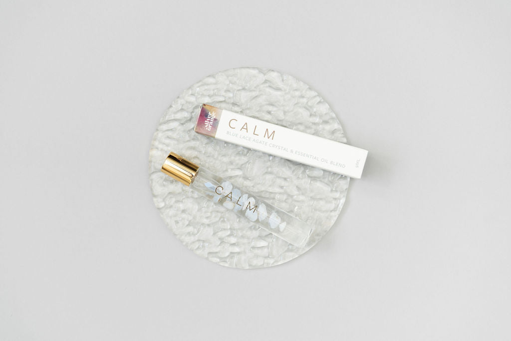 Calm Essential oil Roller bottle blend with a box laying on a clear glass plate on a white background