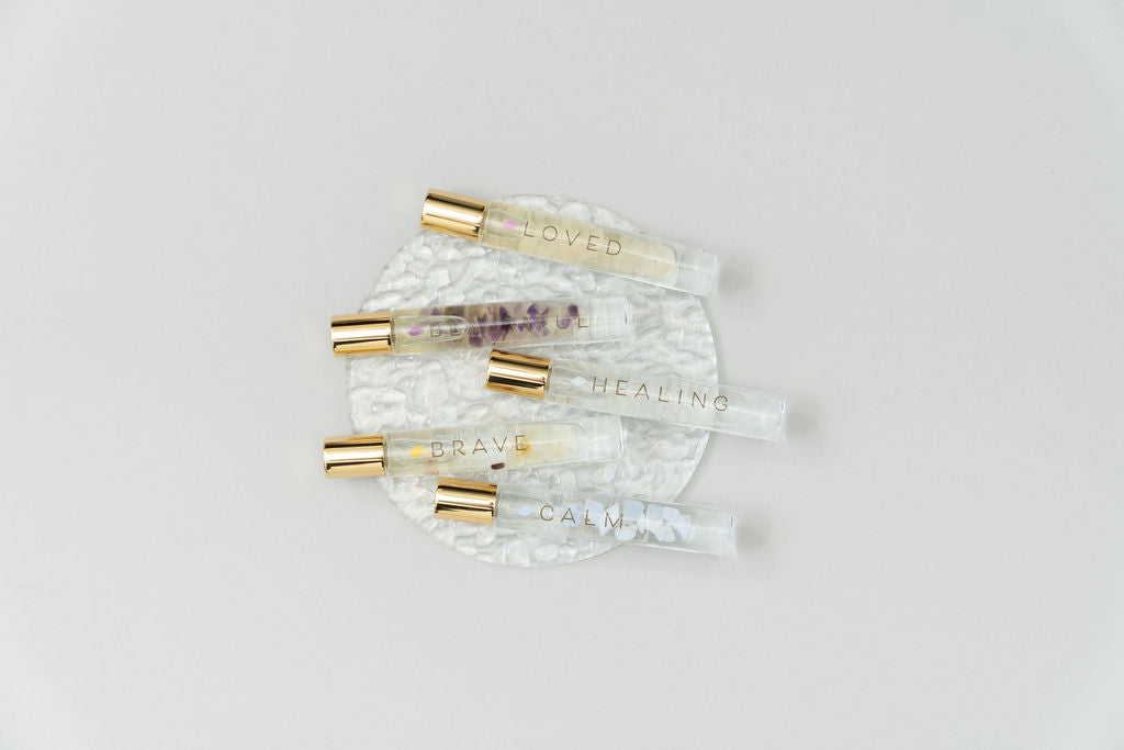5 crystal essential oil blend roller bottles on clear glass plate named Loved, Beautiful, Healing, Brave and Calm