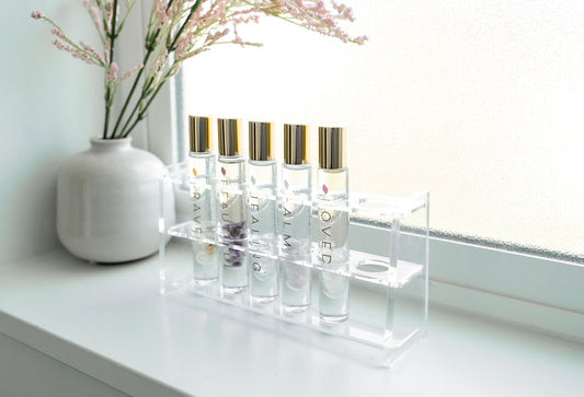 A roller bottle display with natural perfume essential oil blends on a windowsill with a white vase and flowers