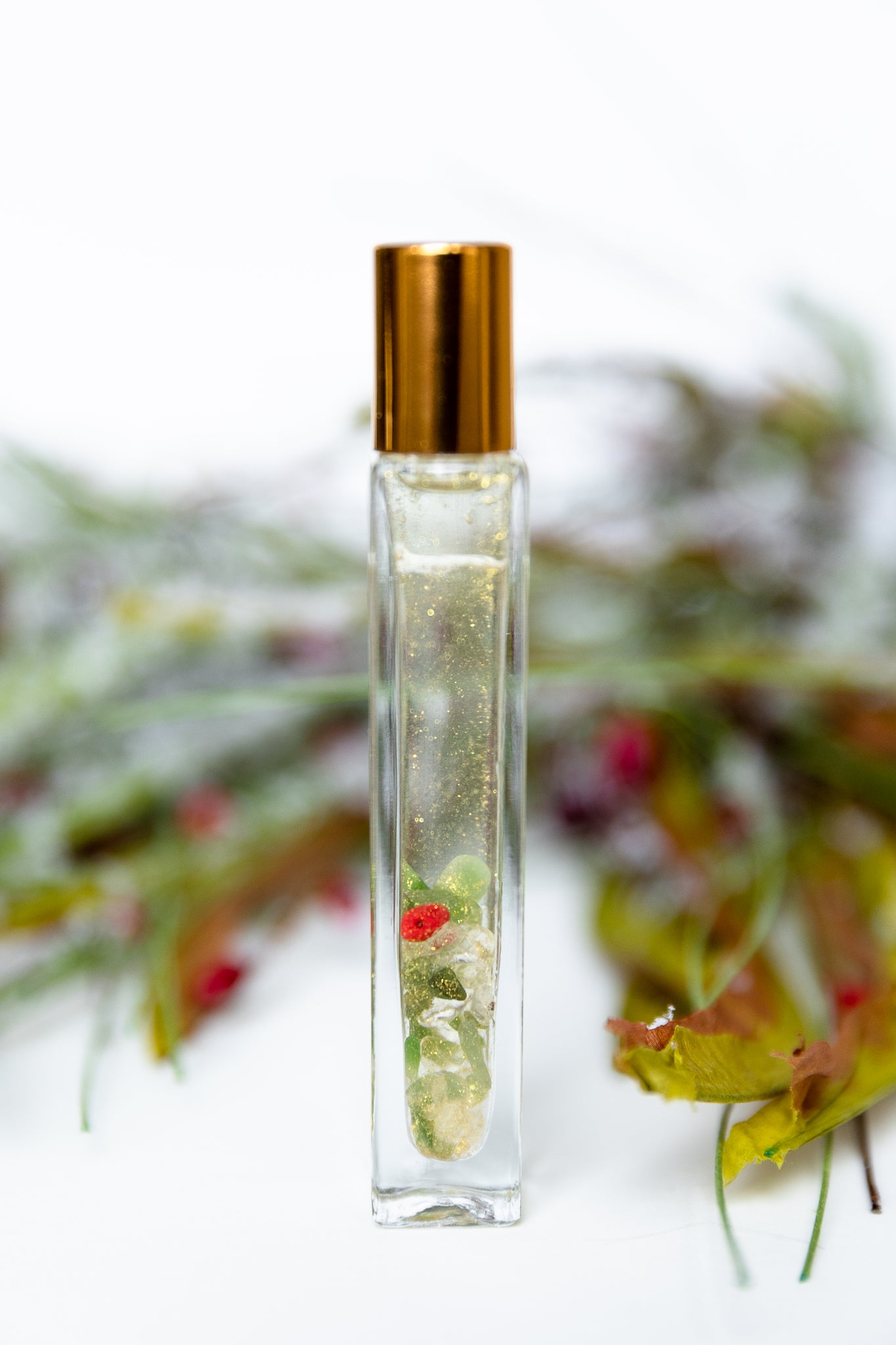 A Glass essential Oil roller bottle with mica shimmer and a gold cap with Christmas leaves and berries on a white background