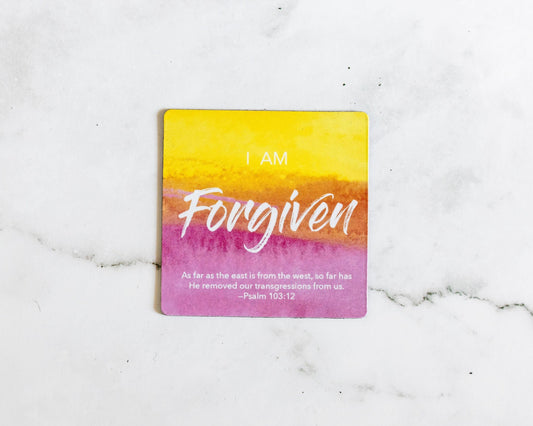 A Pink and Yellow magnet that says I Am Forgiven with a bible verse from Psalm 103:12 on a white marble background that says As far as the east is from the west