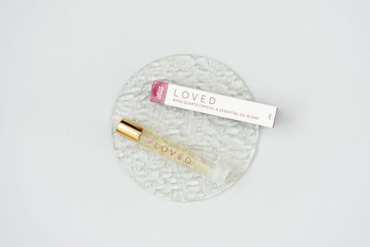 Loved Crystal Essential Oil Roller bottle blend on a clear glass plate with the box