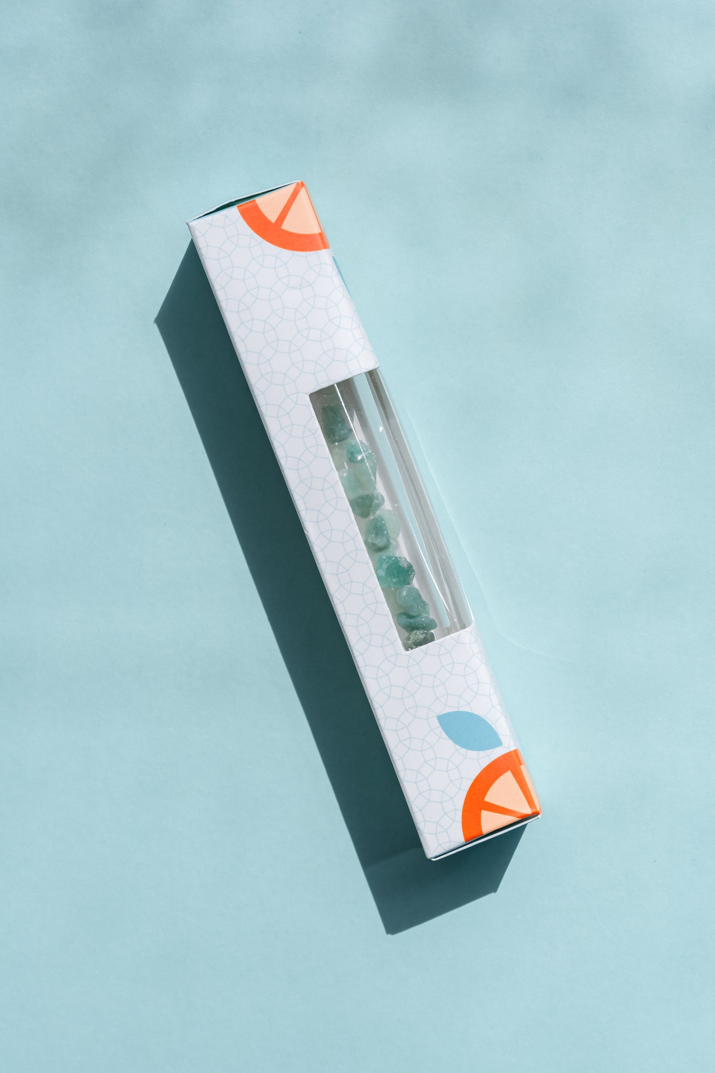 A Roller bottle with Green aventurine stone crystals in a branded box on a pale aqua background