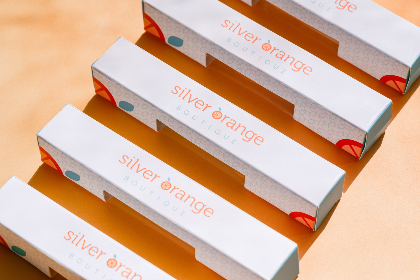 5 Branded Boxes for Roller bottles that say Silver Orange Boutique with logo on pale orange backdrop