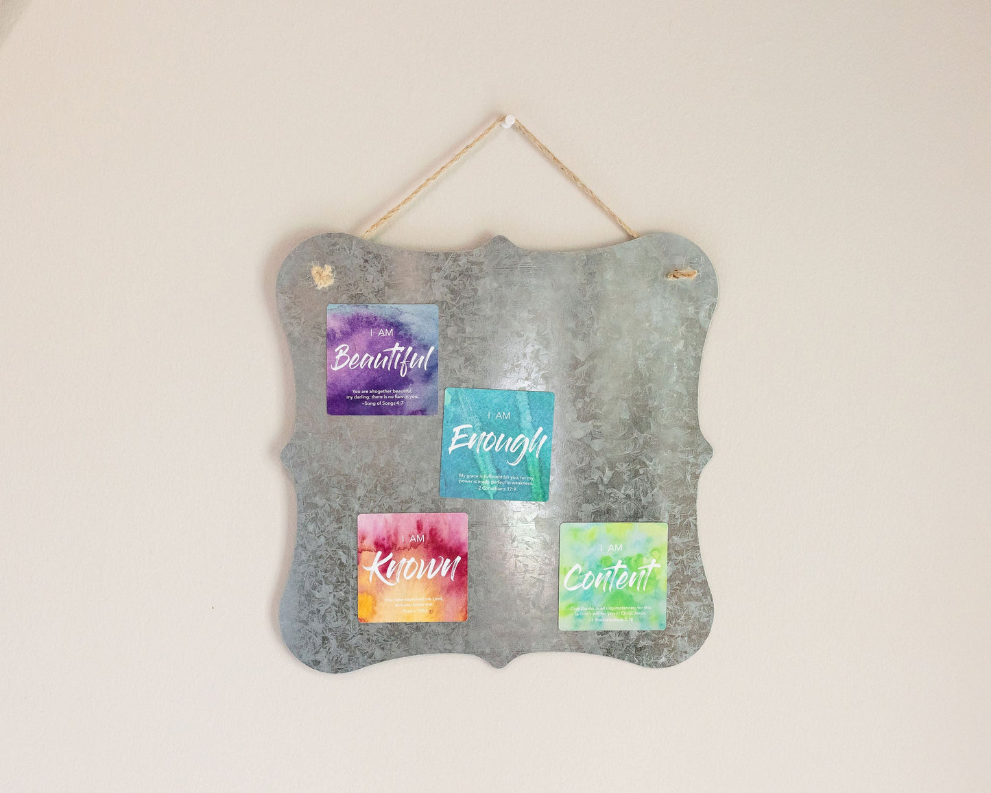 A tin board sign hanging on a wall that has 4 colorful watercolor magnets on it that each say I am Beautiful, I am Enough, I am Known and I am Content