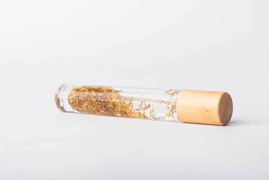 A clear glass roller bottle with Bamboo lid laying on it's side filled with organic calendula flower buds