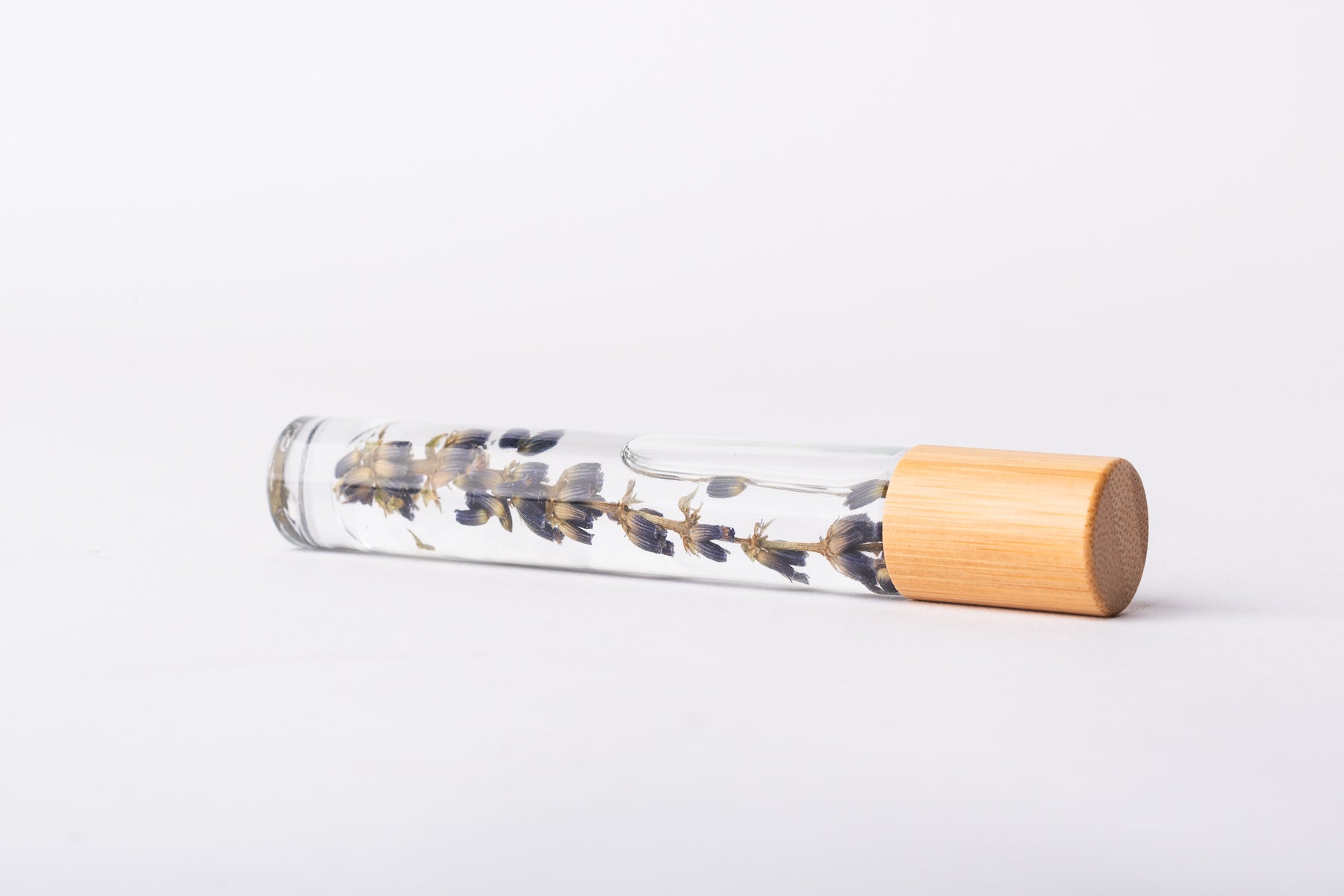 A clear glass roller bottle with Bamboo lid laying on it's side filled with an organic lavender sprig