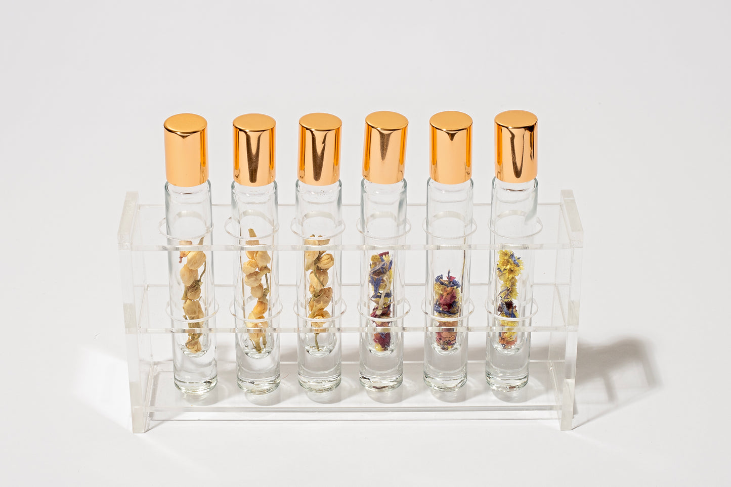 6 clear glass roller bottles in a display stand that contain organic jasmine buds and wildflower mix with gold caps