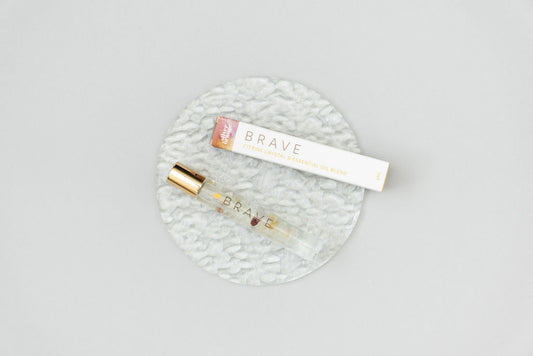A Brave Crystal Essential Oil Roller Bottle Blend on a clear glass plate with the roller box sitting next to it 