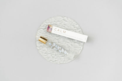 Calm Essential oil Roller bottle blend with a box laying on a clear glass plate on a white background
