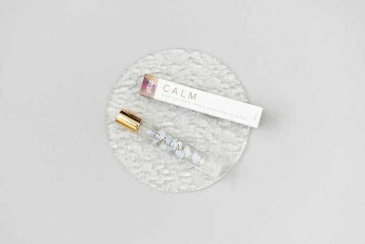 Calm Essential oil Roller bottle blend with a box laying on a clear glass plate on a white background