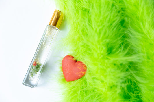 A glass roller bottle with gold mica, green aventurine crystals and red glass heart with green fur on white background and a red grow heart