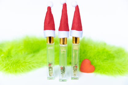 3 glass roller bottles with Santa hats that contain gold mica, green aventurine crystals and red glass heart with green fur on white background and a red grow heart