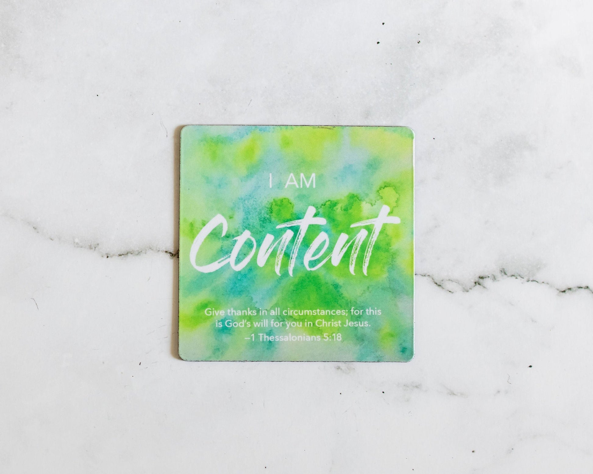 A Green and blue magnet that says I Am Content with a bible verse from I Thessalonians 5:18 on a white marble background that says Give thanks in all circumstances