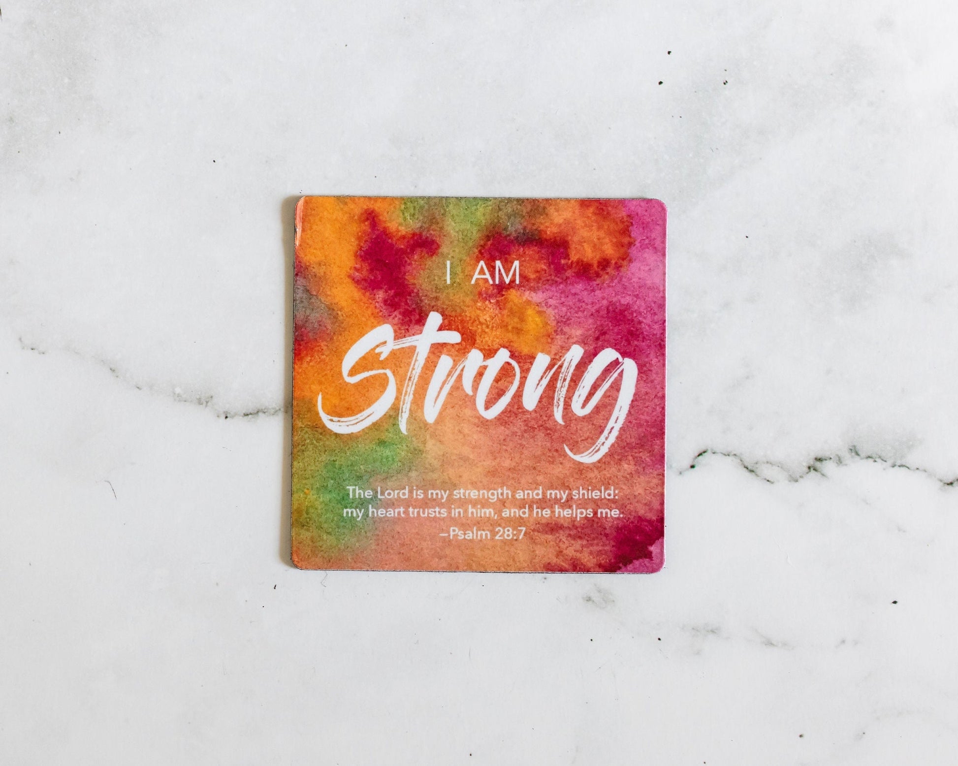 A Pink, orange and green christian bible verse magnet that says I Am Strong with a bible verse from Psalm 28:7 on a white marble background that says The Lord is my strength and my shield