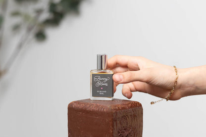 Hand holding a perfume bottle labeled 'Bunny Kisses' on a wooden surface with a blurred natural background